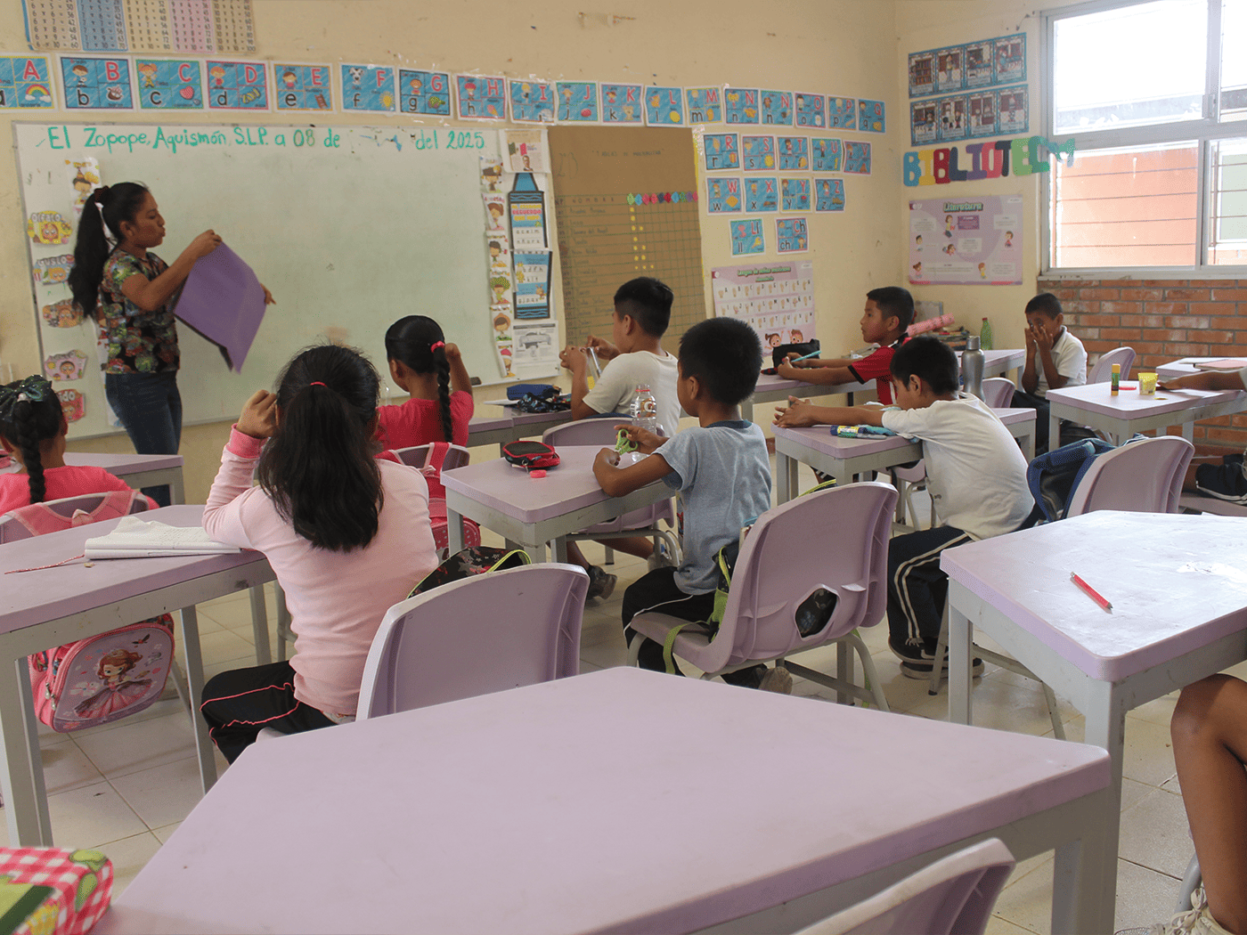 Maestra impartiendo clase con mesas trapezoidales y sillas Bravo Memosa en primaria, mobiliario del Programa La Escuela es Nuestra.